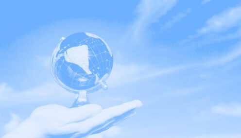 Blue washed feminine hand holding globe against a beautiful blue sky.