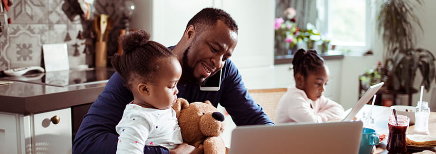 Man works on laptop whilst spending time with his tow young kids 