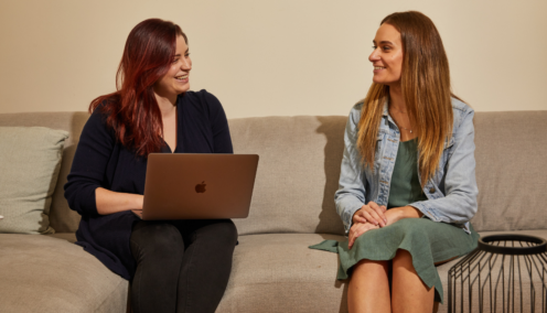 two women sitting on a sofa with an laptop