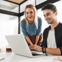 This is an image of 2 people smiling and looking at a laptop.