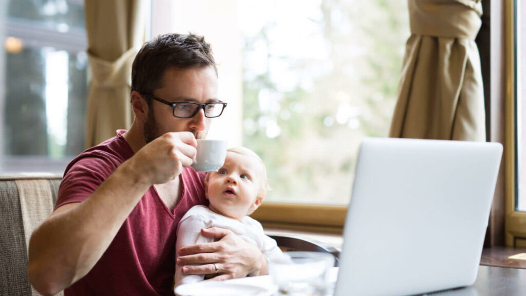 Image of a father working remotely while holding his child