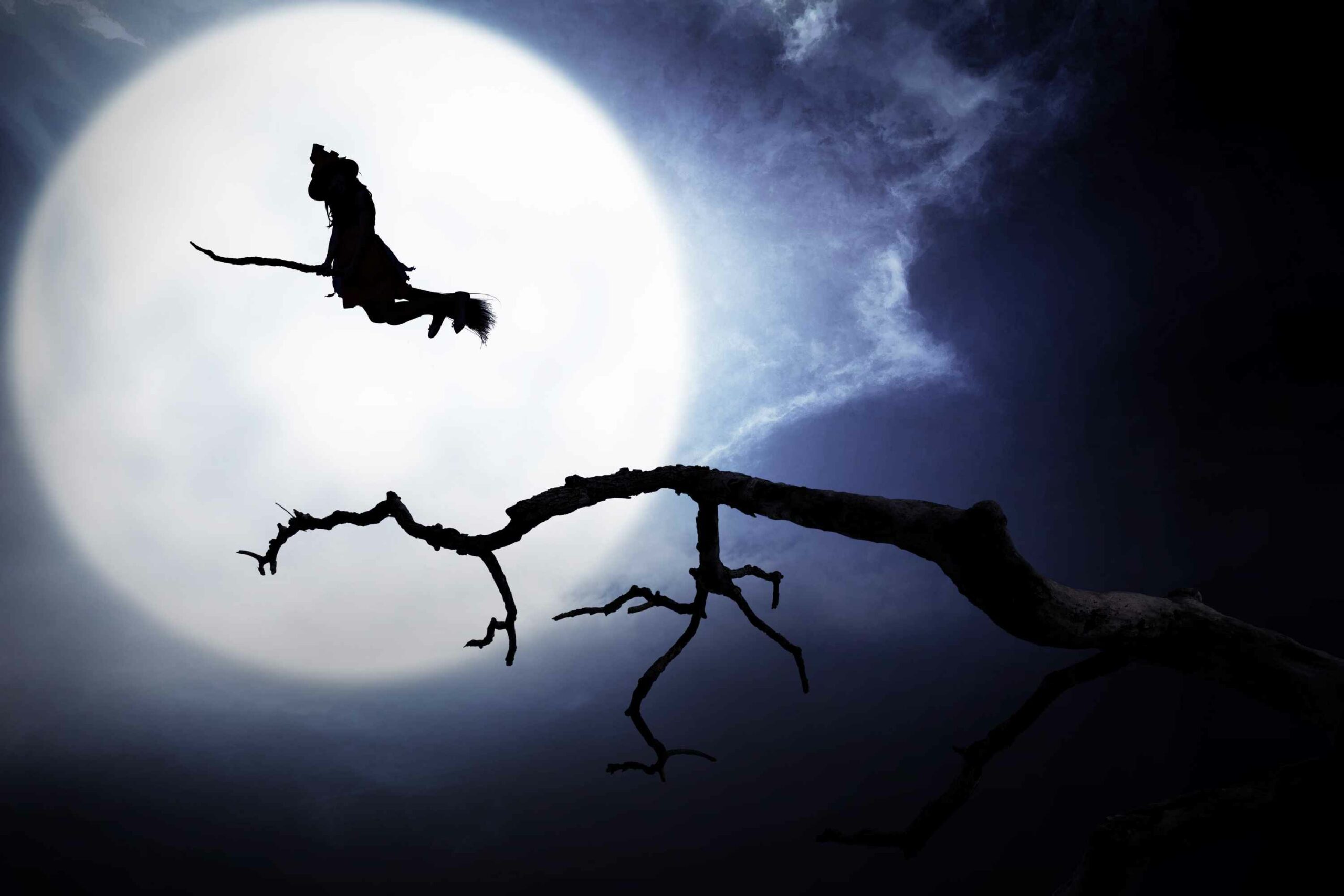 Witch on broomstick flying in front of moon at night