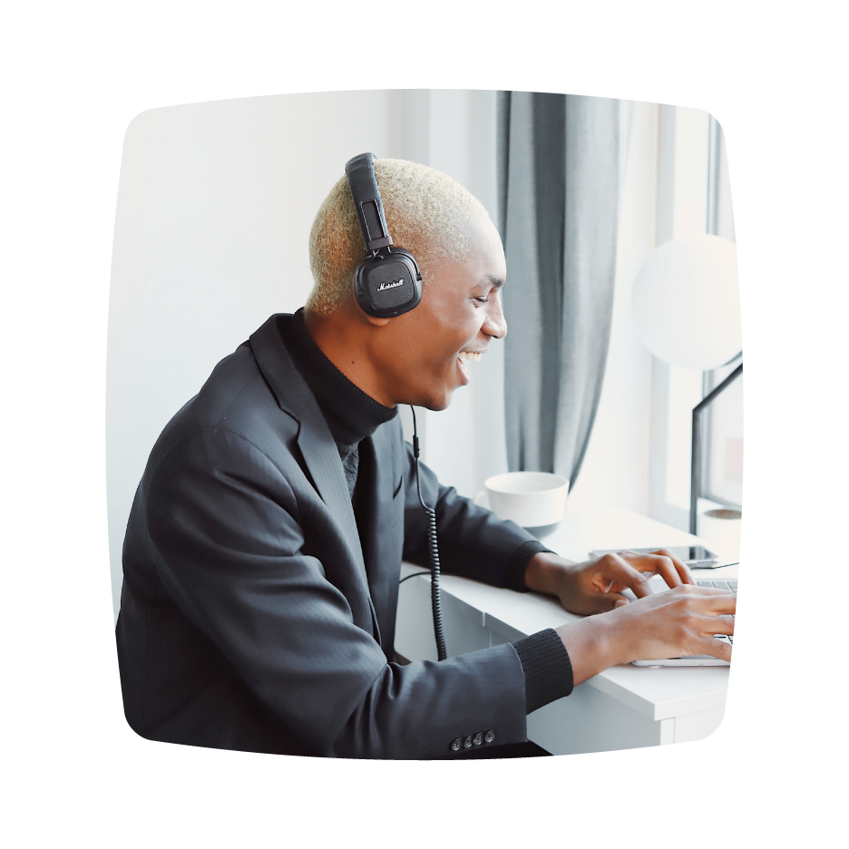 A photo of a person wearing headphones, smiling while working on a laptop at a desk