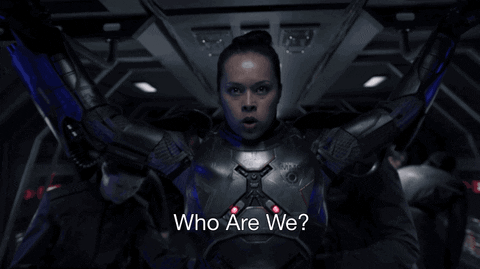 
The GIF depicts a scene of a person in a futuristic suit raising their arms in a dramatic gesture, with the caption "Who Are We?" displayed at the bottom. The setting appears to be inside a spaceship or high-tech environment