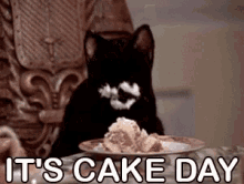 Black cat with its face covered in frosting or cream, sitting at a table with a plate of cake in front of it, and the text 'IT'S CAKE DAY' displayed at the bottom