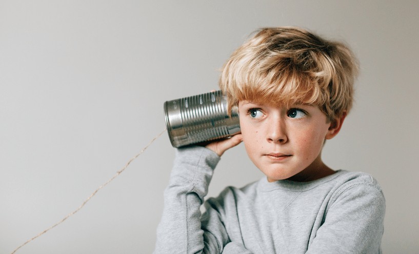 A small boy holding a can up against his ear