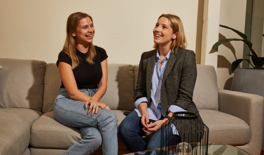 Two women having a conversation on a grey couch