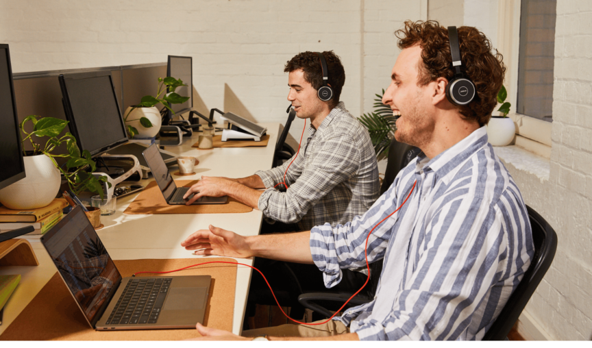 Two men looking at laptops, wearing headsets