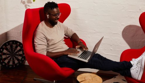 guy seated on a loungechair smiling and using his computer