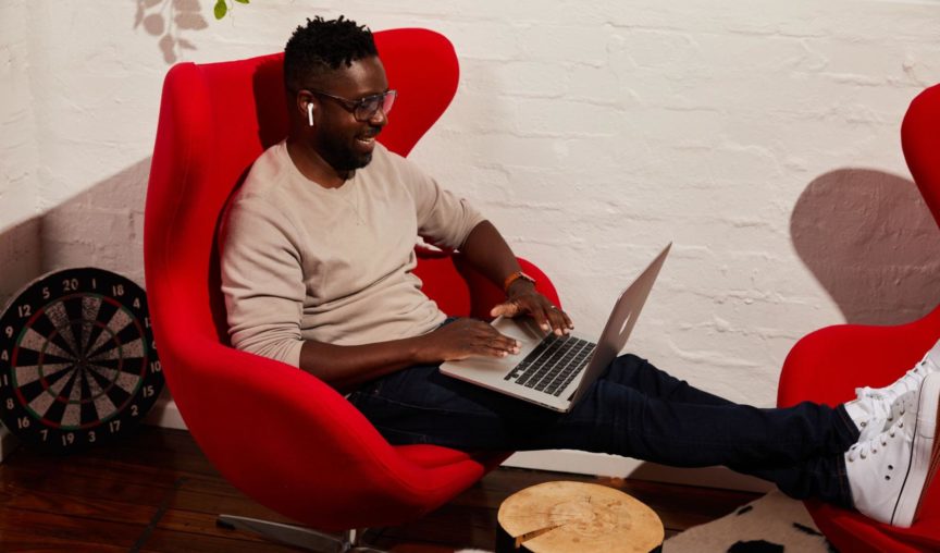 guy seated on a loungechair smiling and using his computer