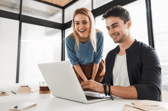 This is an image of 2 people smiling and looking at a laptop.