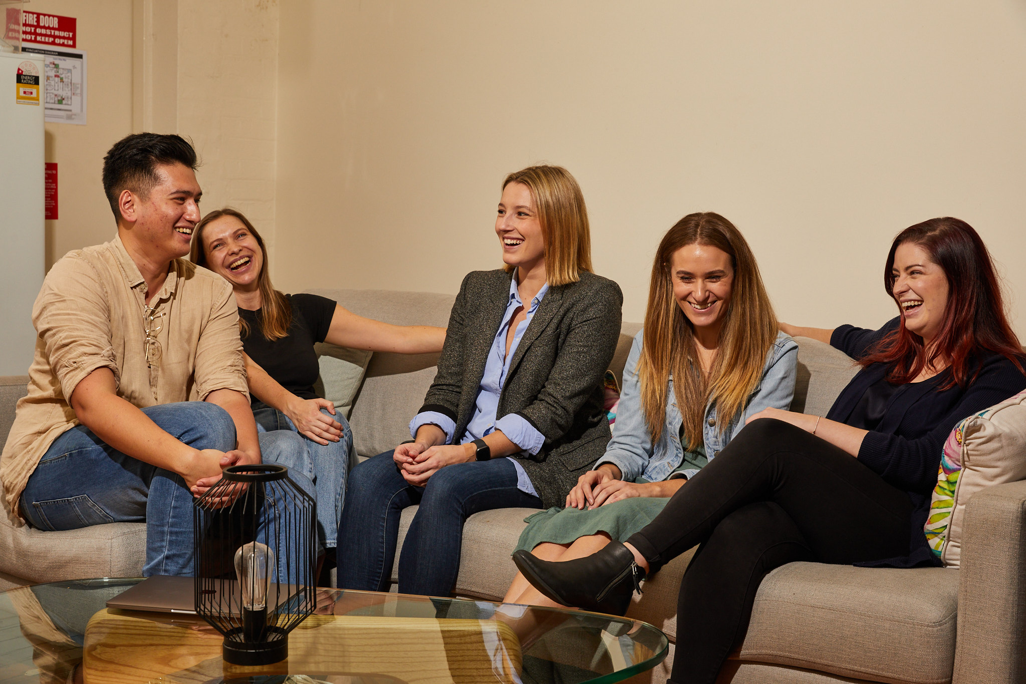 A group of five people sitting on a couch, laughing and enjoying a conversation in a relaxed, indoor setting