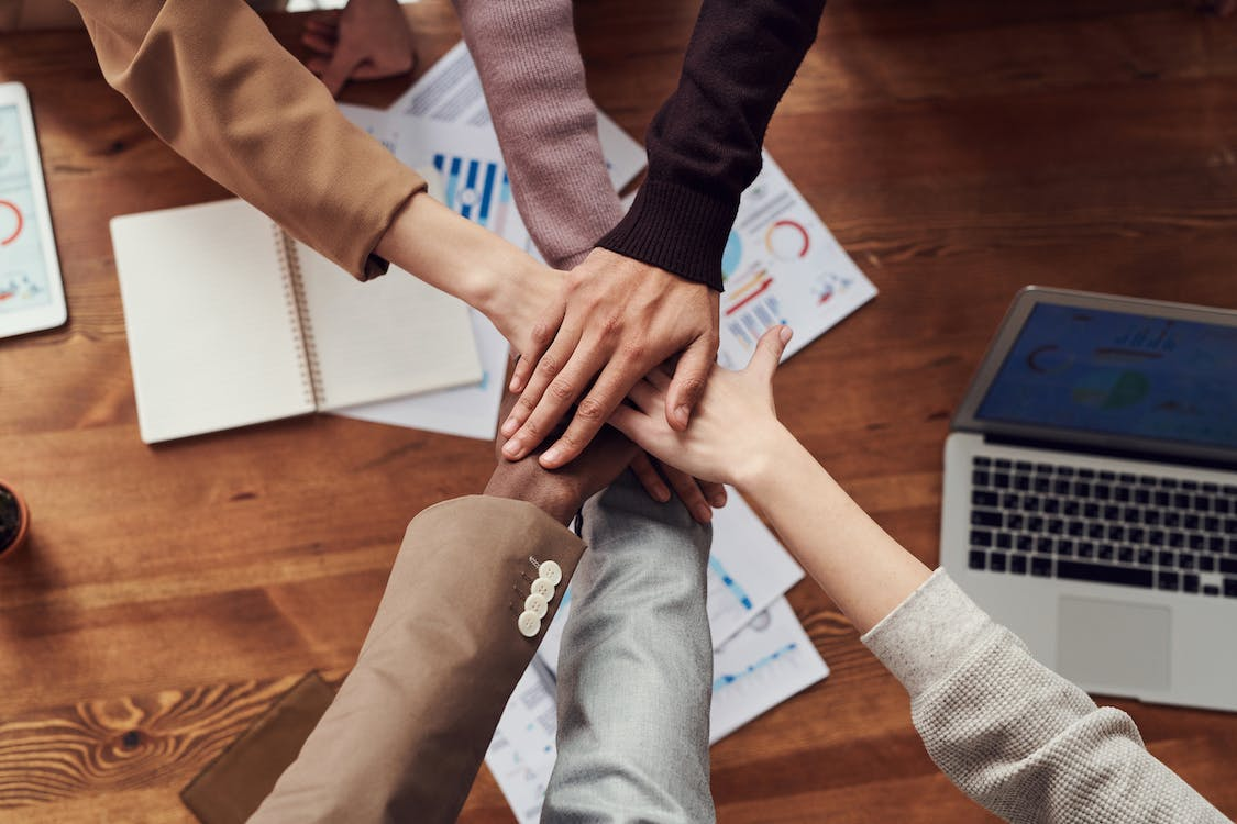 group of diverse employees all putting their hands together in the middle of the table