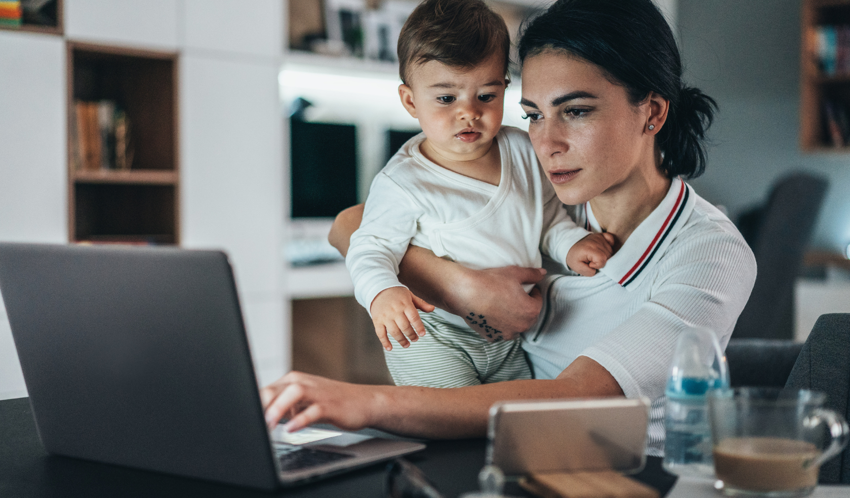 woman holding her kid whilst working from home 