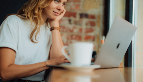 A woman sits in a cafe, looking at her laptop with a mug of coffee next to her