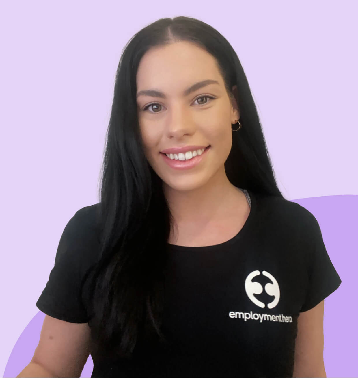 A woman smiling, wearing a black t-shirt with the Employment Hero logo, in front of a light purple background
