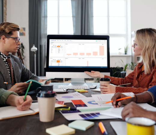 A photo of a group of people sitting around a table in a meeting room, discussing data displayed on a large computer screen