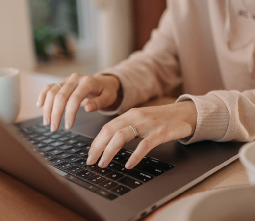 A woman types on a laptop, only hands visible