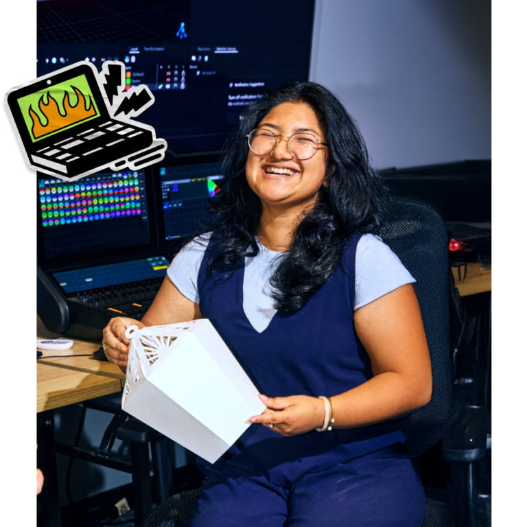 A bright, lifestyle photograph of a smiling woman with curly hair, wearing a light blue sweater. She is seated at a table, holding a paper document in one hand while happily looking at a silver laptop screen. A glass of water and a smartphone rest on the table beside her.