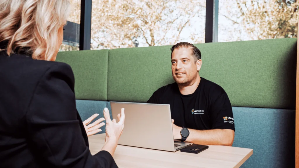 Two professionals sitting in a green office booth having a collaborative discussion over a laptop, illustrating team alignment for End of Financial Year HR and payroll planning.