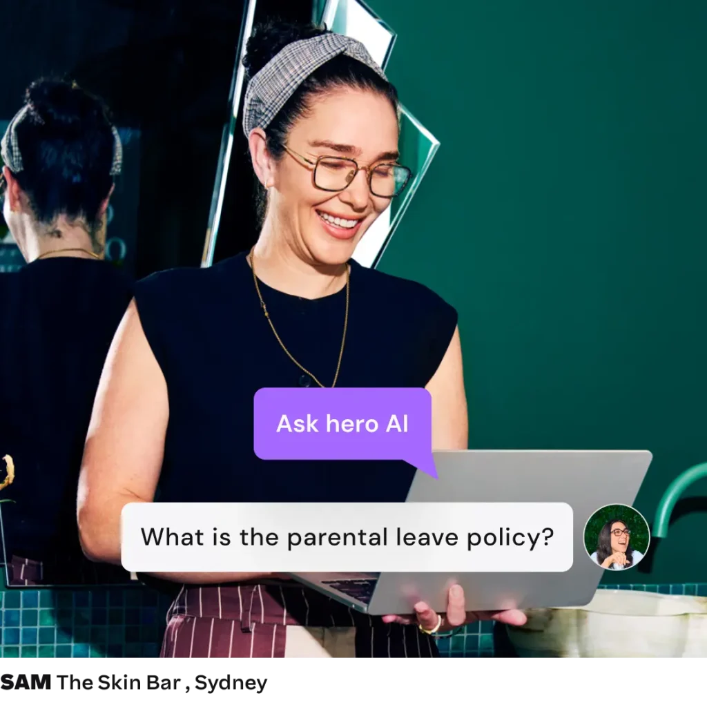 Smiling woman using a laptop with an on-screen prompt asking Hero AI about the parental leave policy.