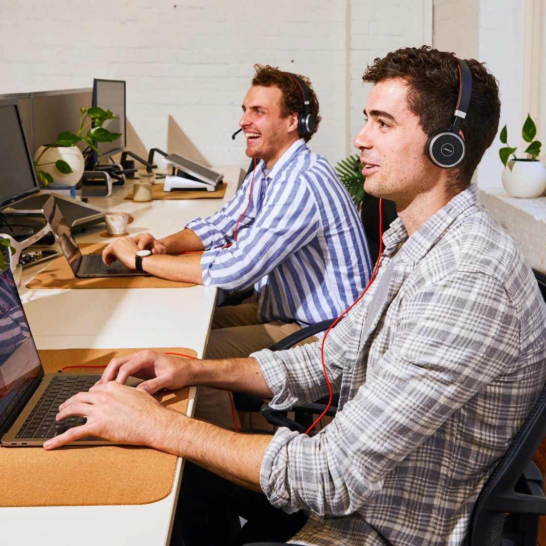 Two men wearing headsets working on laptops at a bright, modern customer support office.