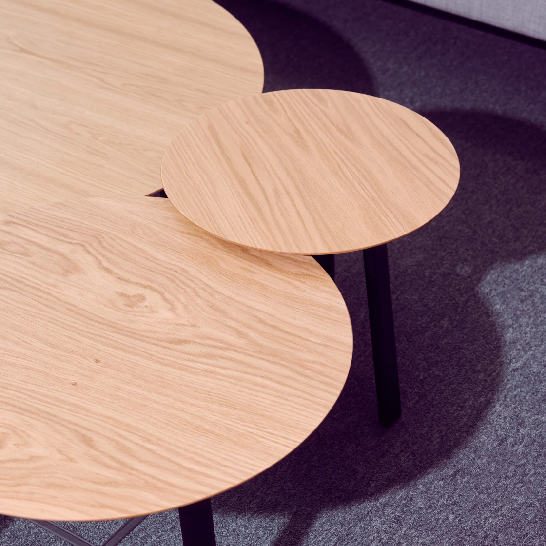 A set of nested round wooden tables with black legs placed on a carpeted floor.