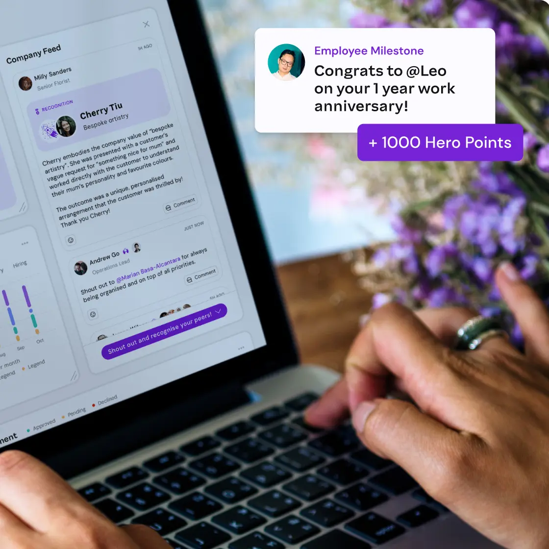A person interacts with a digital company feed on a laptop, displaying peer recognition and a congratulatory work anniversary message with hero points.