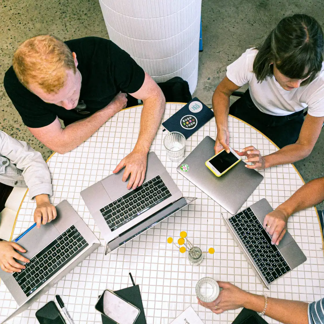 A group of diverse individuals seated at a table, each using laptops, engaged in discussion or collaboration.