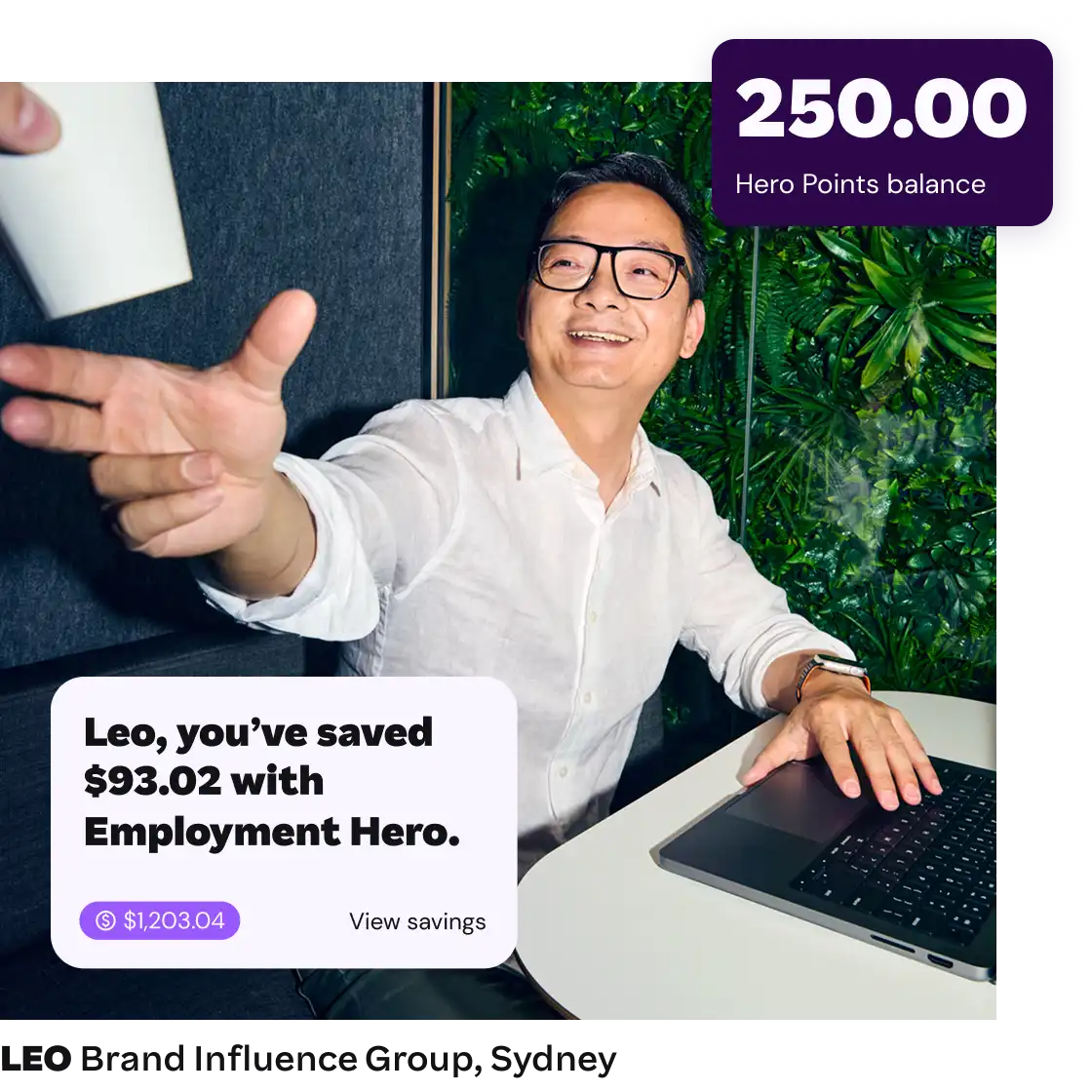 Man in a white shirt smiling and reaching for a coffee cup, sitting at a table with a laptop. Text overlay shows savings and Hero Points balance. Bright, cheerful mood.