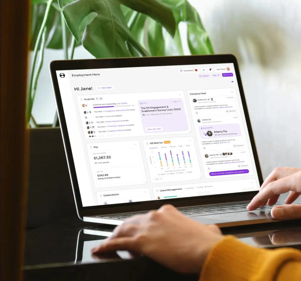 Person using a laptop displaying a dashboard with tasks, surveys, and metrics in a bright office setting. Lush green plant in the background.