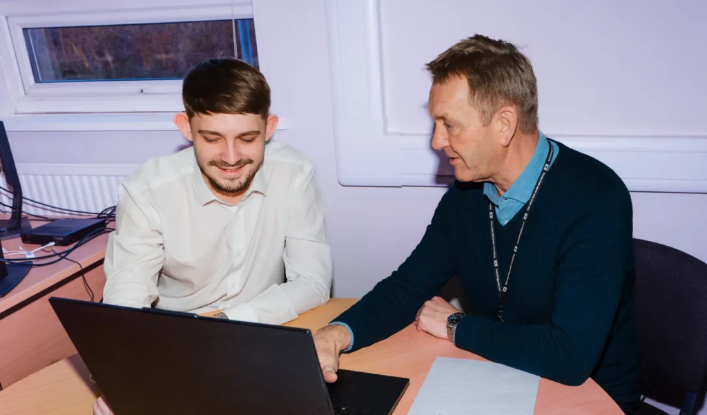 Two men collaborating and smiling while working on a laptop.