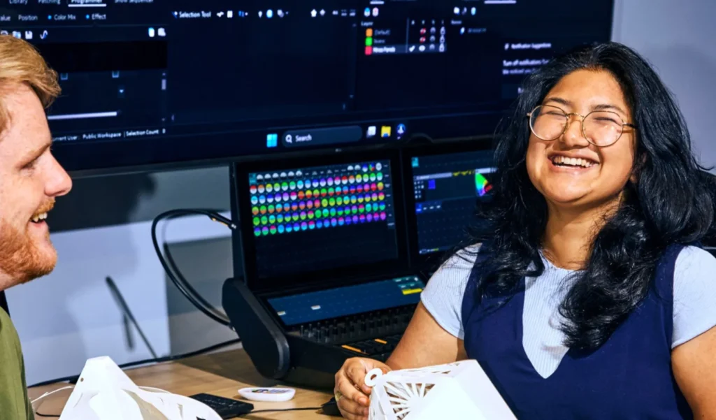 Two people smiling and laughing together while sitting in front of a computer screen.