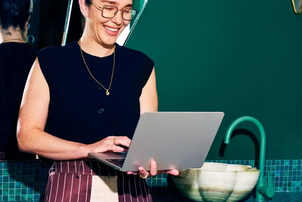 A smiling woman using a laptop in a modern workspace, representing productivity with OKR templates.