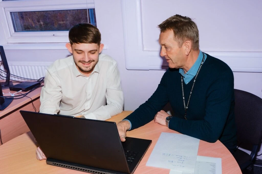Two male colleagues collaborating at a laptop, symbolizing the essential training and support needed to ensure HR compliance for small business employees.