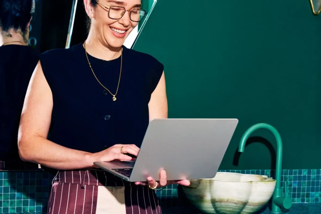 A smiling woman using a laptop in a modern workspace, representing superannuation and paid parental leave processes.