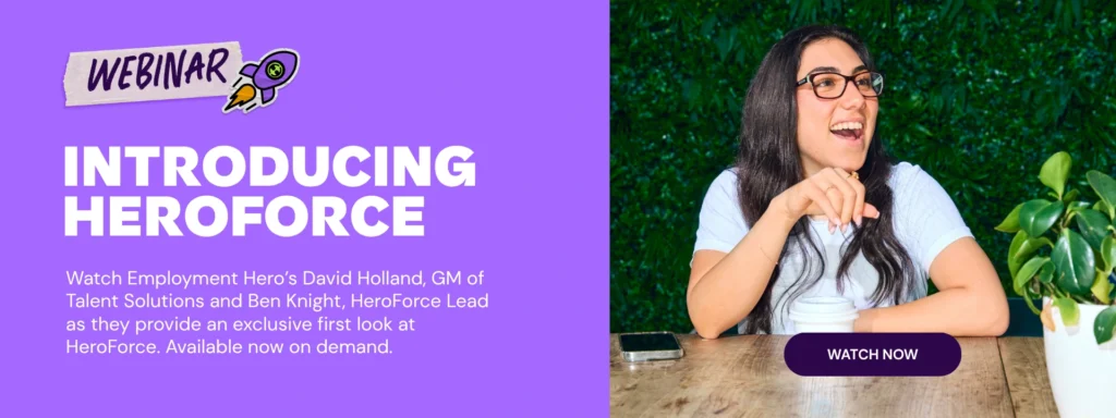 A woman with glasses smiles at a wooden table surrounded by plants against a green backdrop. Text reads "Webinar: Introducing HeroForce. Watch now."