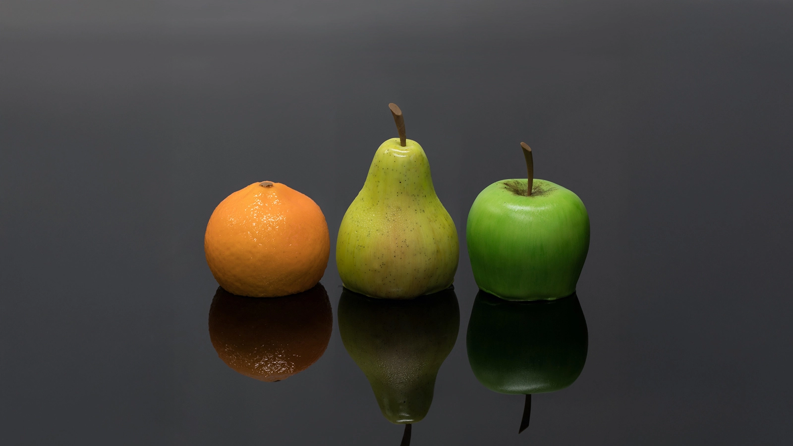 A still-life arrangement featuring an orange, a yellow-green pear, and a bright green apple standing on a dark, reflective surface.