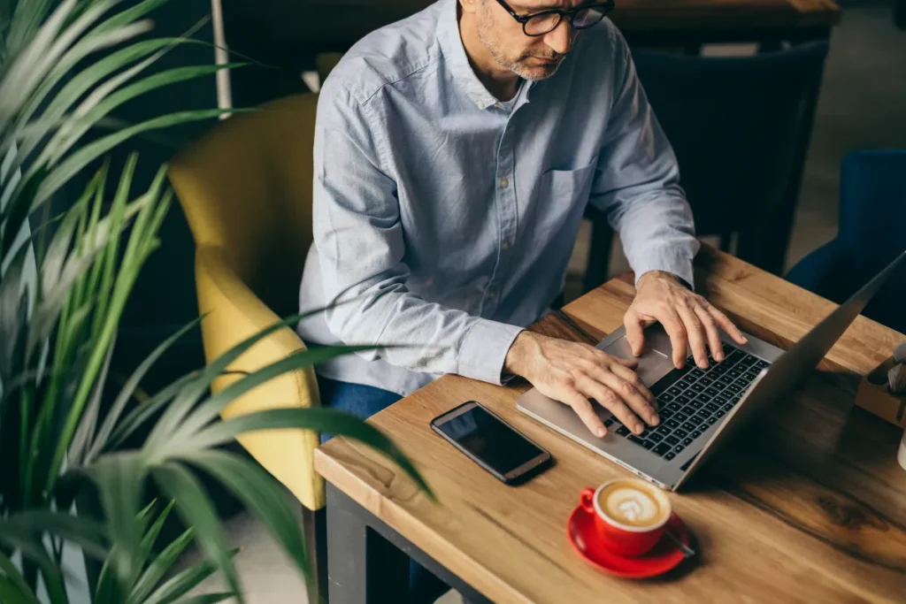 Man typing on his laptop with coffee on the table