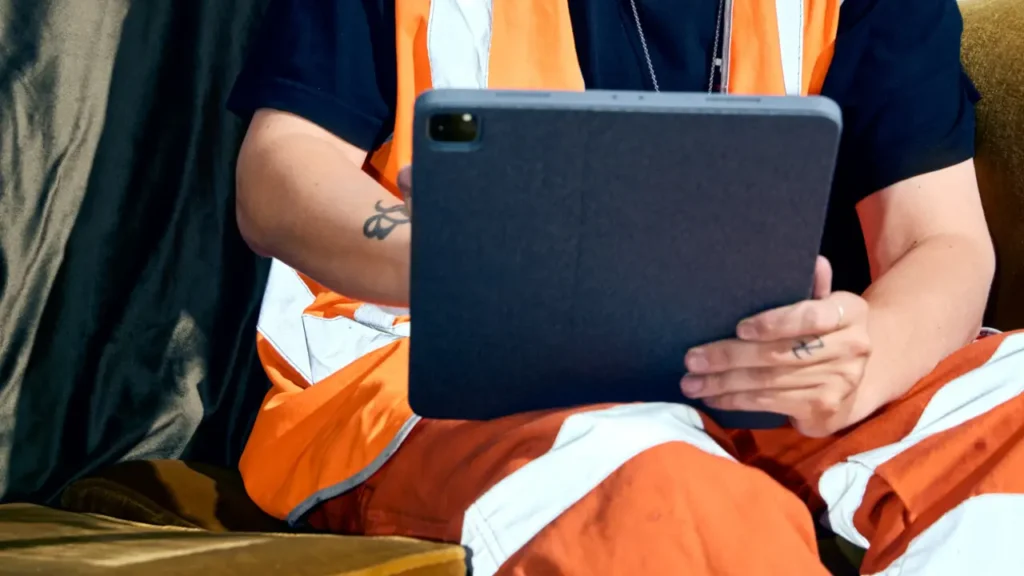 A person in a high-visibility orange safety vest and pants using a tablet computer.