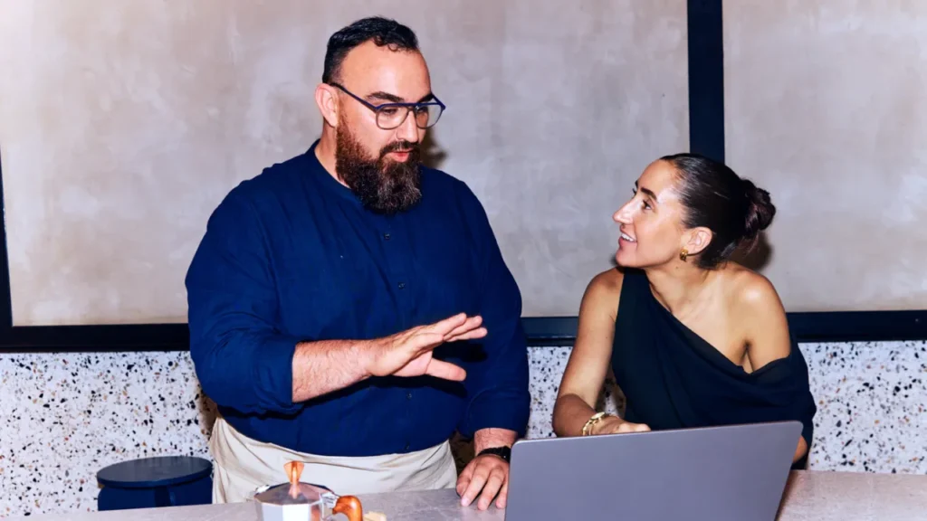 A manager and employee collaborating in front of a laptop, representing the collaborative process of designing an employee work schedule.