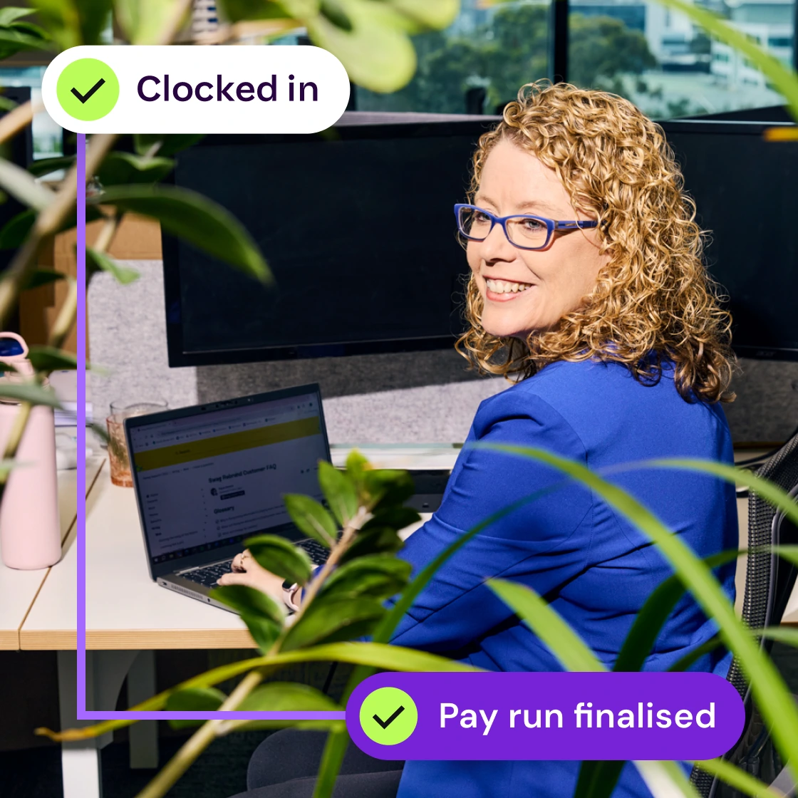 Smiling person with curly hair working on a laptop in an office, surrounded by plants. Overlay text reads “Clocked in” and “Pay run finalised.”