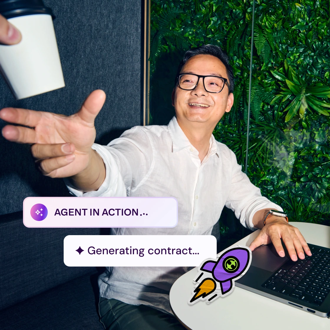A man in a white shirt with glasses smiles while receiving a coffee cup. Text bubbles read "Agent in Action" and "Generating contract," conveying a positive, dynamic work atmosphere with a laptop and green plant wall in the background.