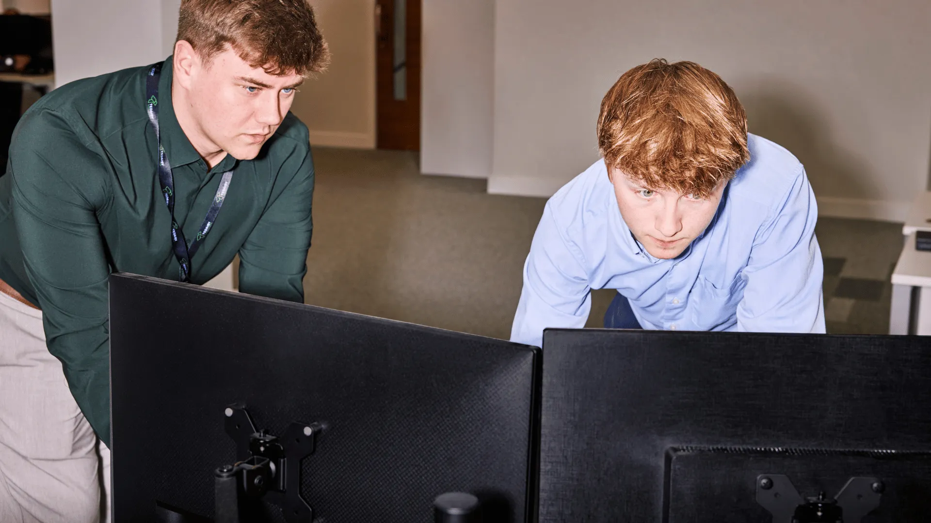 Two young male professionals closely reviewing information on dual computer monitors, representing employers managing and submitting employee super contributions through a superannuation clearing house.