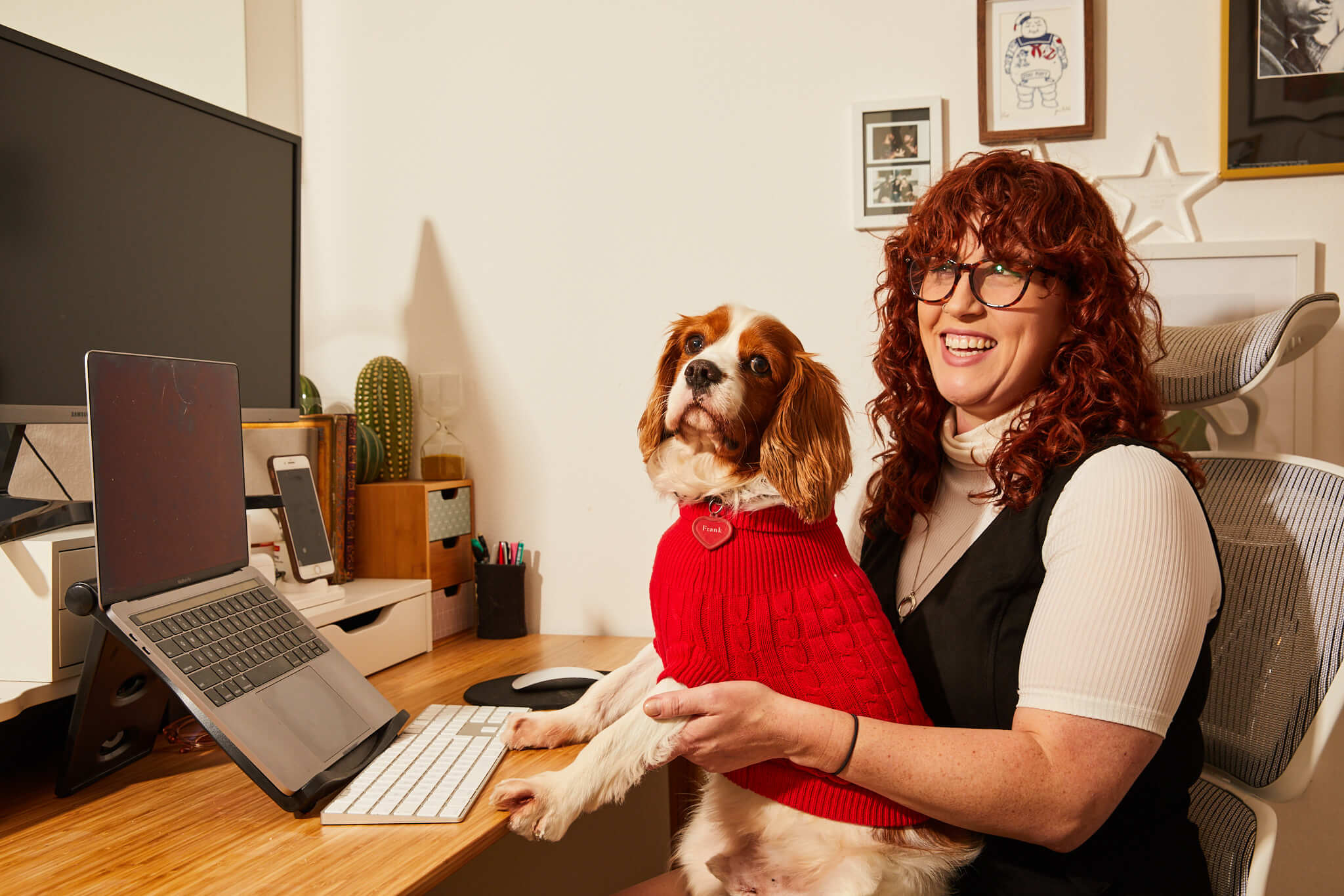 Woman sitting at home desk holding a dog in a red vest